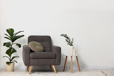 Photo of Comfortable armchair, pillow, side table and green houseplants indoors, space for text