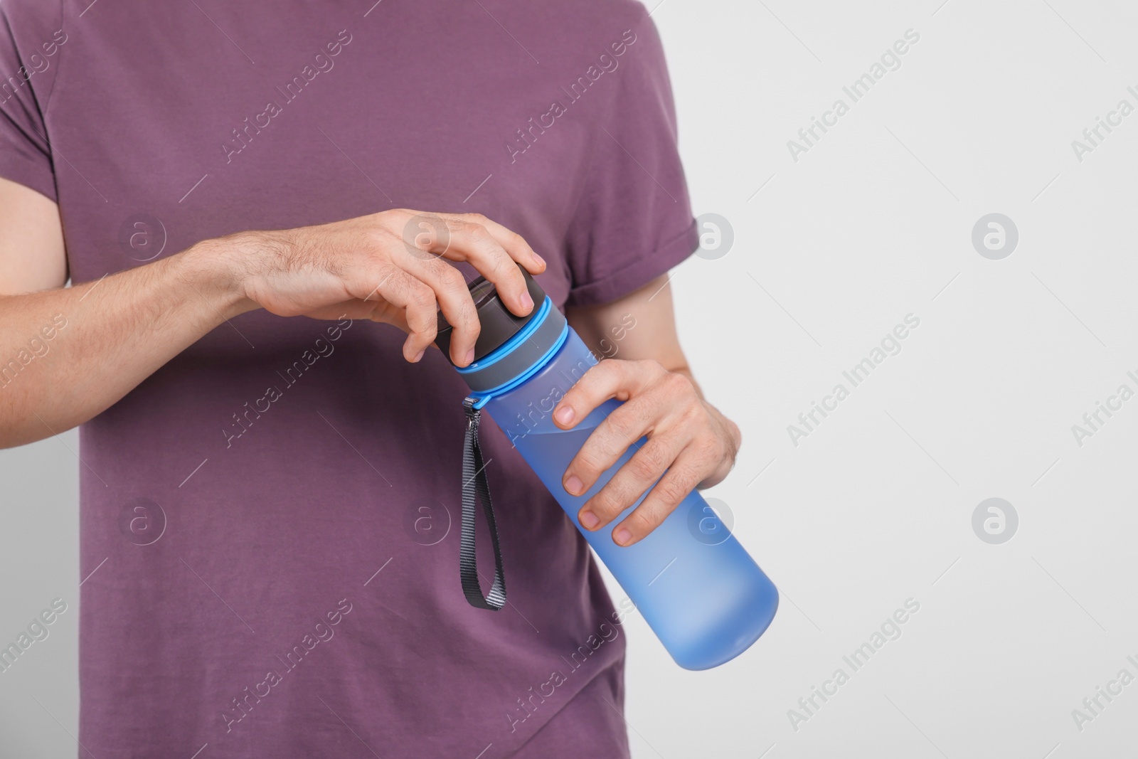 Photo of Man holding transparent plastic bottle with drink on light grey background, closeup. Space for text