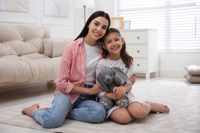 Portrait of happy young mother and her daughter on floor in living room. Adoption concept