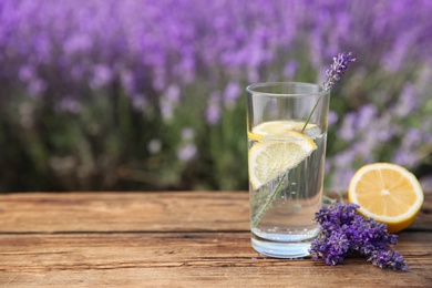 Lemonade with lemon slices and lavender flowers on wooden table outdoors, closeup. Space for text