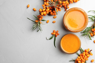 Photo of Delicious sea buckthorn jam and fresh berries on light grey table, flat lay. Space for text