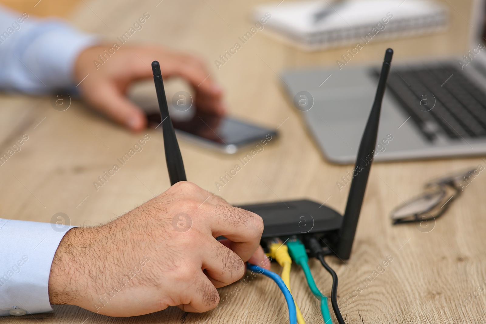 Photo of Man inserting cable into Wi-Fi router at wooden table indoors, closeup