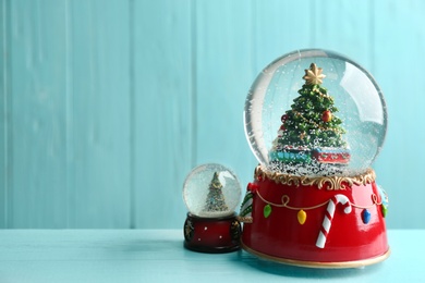 Photo of Beautiful snow globes with Christmas trees on light blue wooden table, space for text
