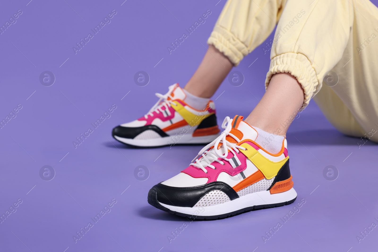 Photo of Woman wearing pair of new stylish sneakers on purple background, closeup