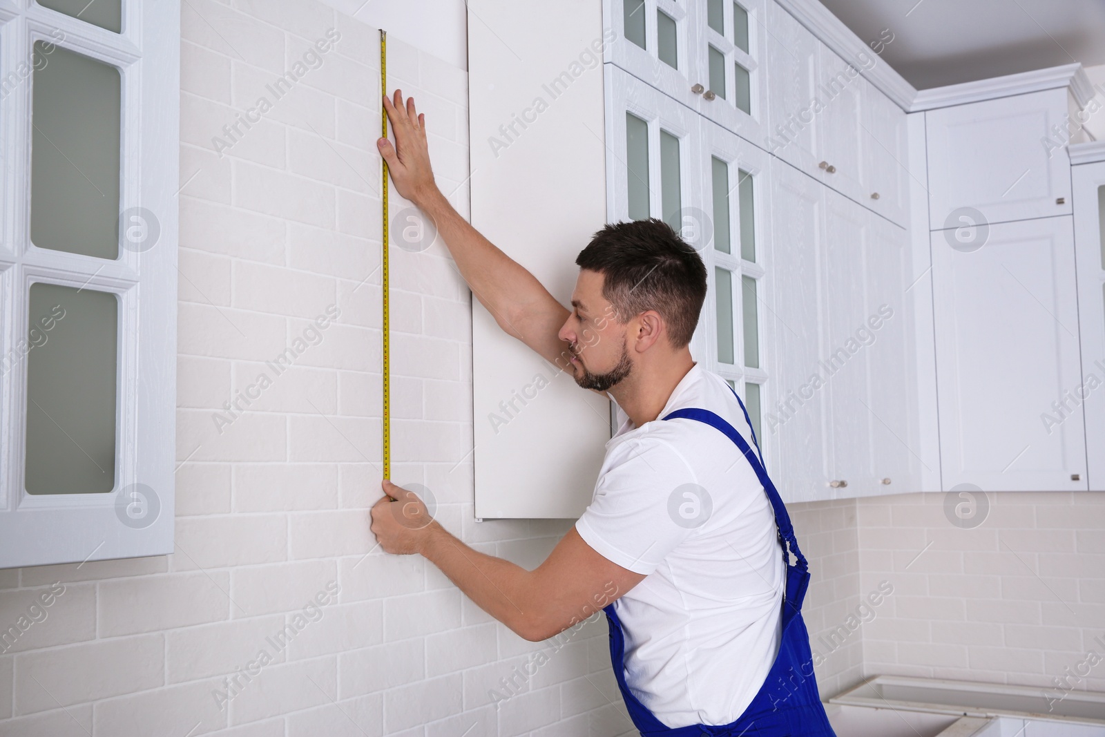 Photo of Worker using measuring tape while installing new furniture in kitchen