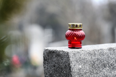 Photo of Lamp with candle on grey granite tombstone outdoors, space for text. Funeral ceremony