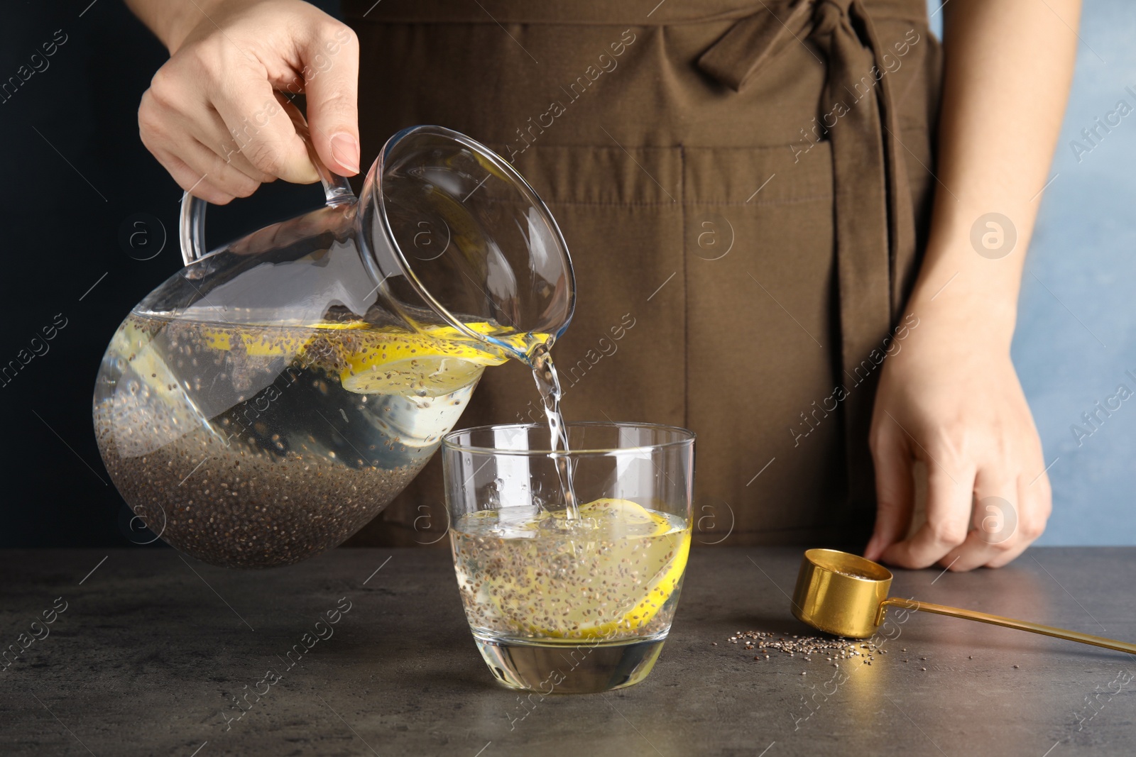 Photo of Young woman pouring water with chia seeds and lemon into glass at table, closeup