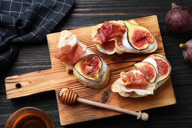 Photo of Sandwiches with ripe figs, prosciutto and cream cheese served on black wooden table, flat lay