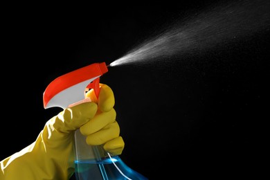 Photo of Woman spraying liquid from bottle on black background, closeup