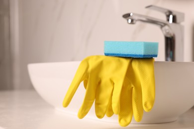 Photo of Sponge and rubber gloves on bathroom sink indoors, closeup. Space for text