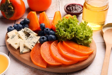 Delicious persimmon, blue cheese and blueberries on tiled surface, closeup