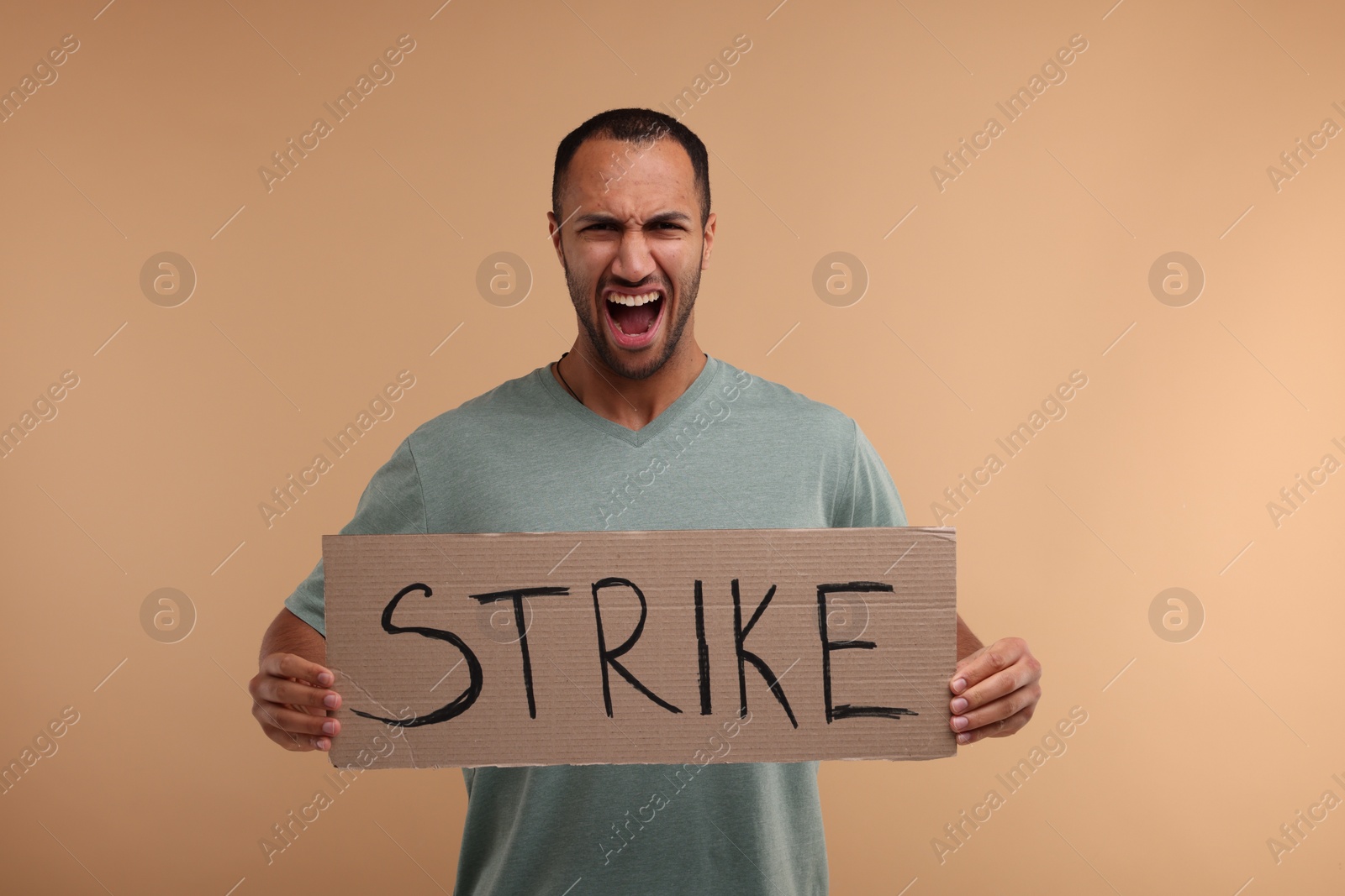 Photo of Angry man holding cardboard banner with word Strike on beige background