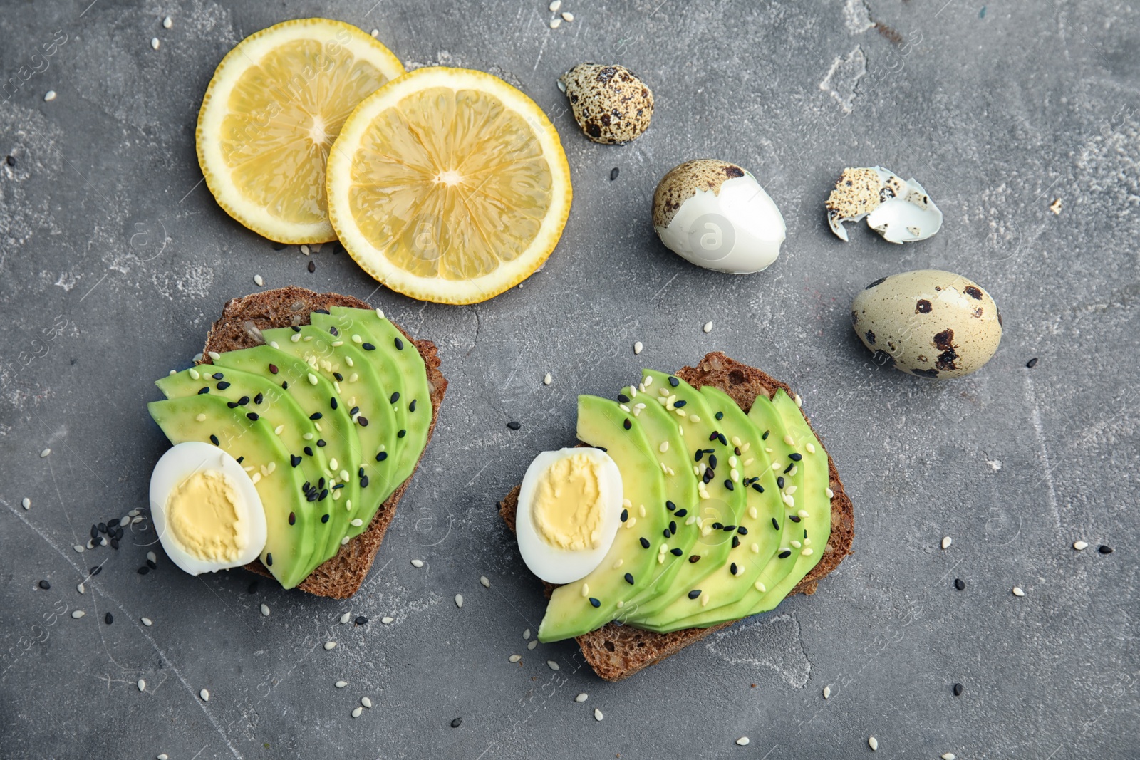 Photo of Rye toasts with sliced avocado and quail eggs on table, top view