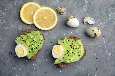Rye toasts with sliced avocado and quail eggs on table, top view
