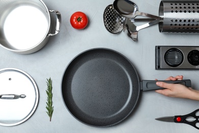 Photo of Woman holding frying pan over table with clean cookware, top view