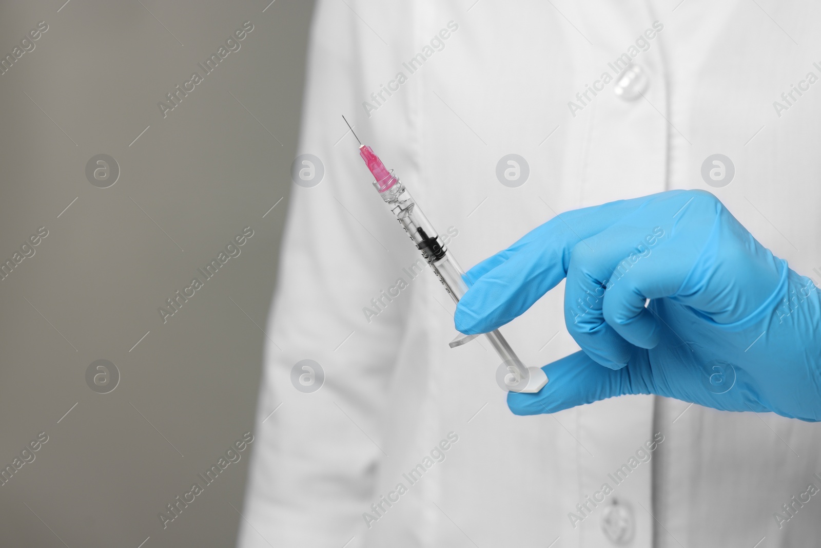 Photo of Doctor holding syringe on grey background, closeup. Space for text