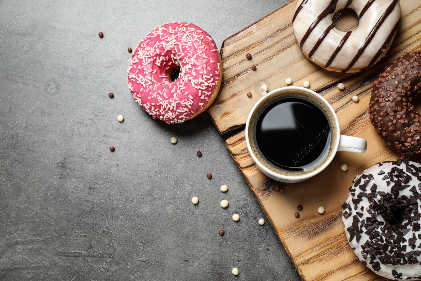 Photo of Yummy donuts with sprinkles and coffee on grey table, flat lay. Space for text