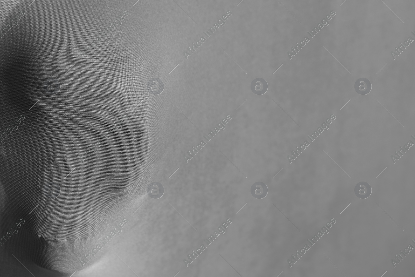 Photo of Silhouette of creepy ghost with skull behind cloth, space for text. Black and white effect