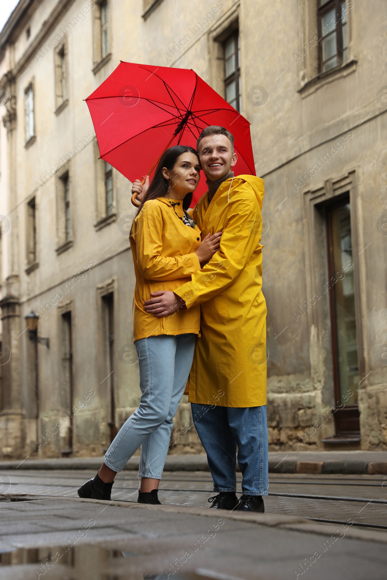 Photo of Lovely young couple with red umbrella together on city street