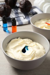 Photo of Bowls of different cream with food coloring on white wooden table