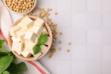 Photo of Delicious tofu cheese, basil and soybeans on white tiled table, flat lay. Space for text