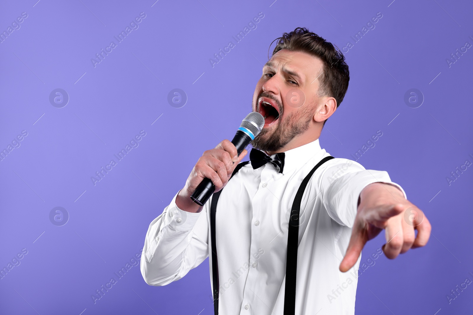 Photo of Handsome man with microphone singing on violet background. Space for text