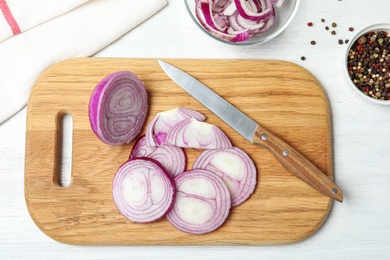 Wooden board with cut red onion and knife on white table, flat lay