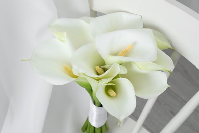 Photo of Beautiful calla lily flowers on white chair indoors, closeup