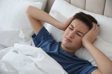 Photo of Cute teenage boy suffering from headache while lying in bed at home