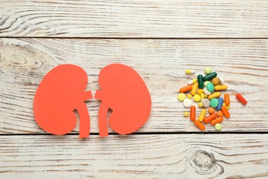 Photo of Paper cutout of kidneys and pills on white wooden table, flat lay