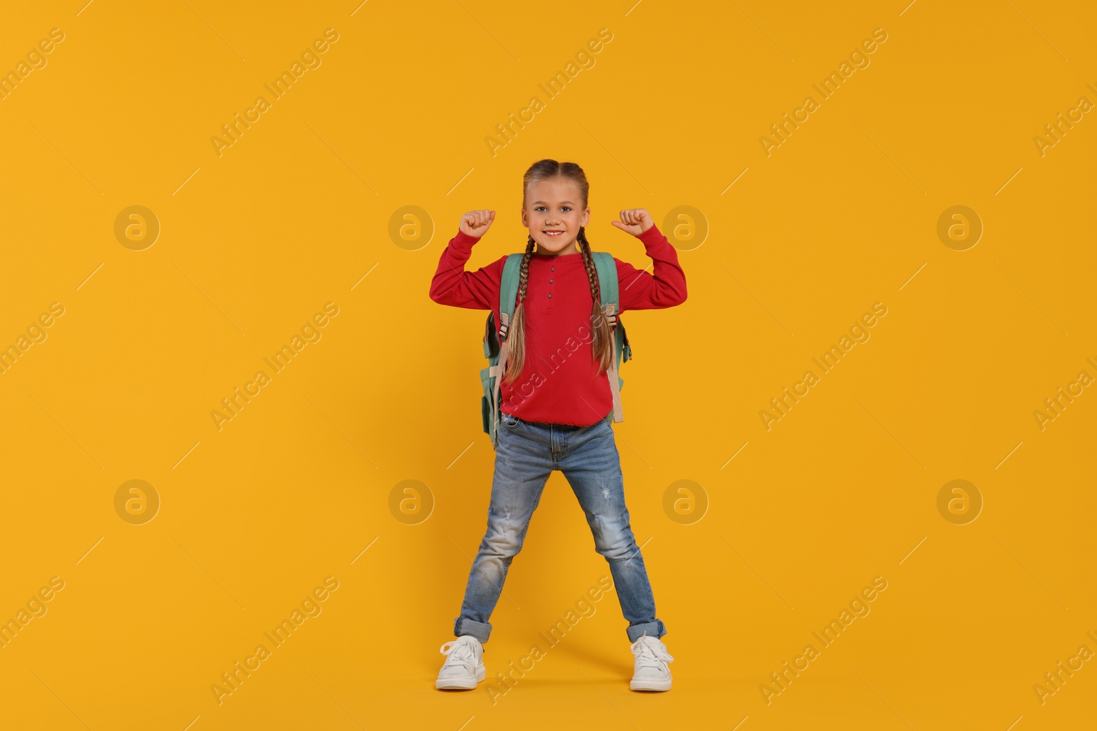 Photo of Happy schoolgirl with backpack on orange background