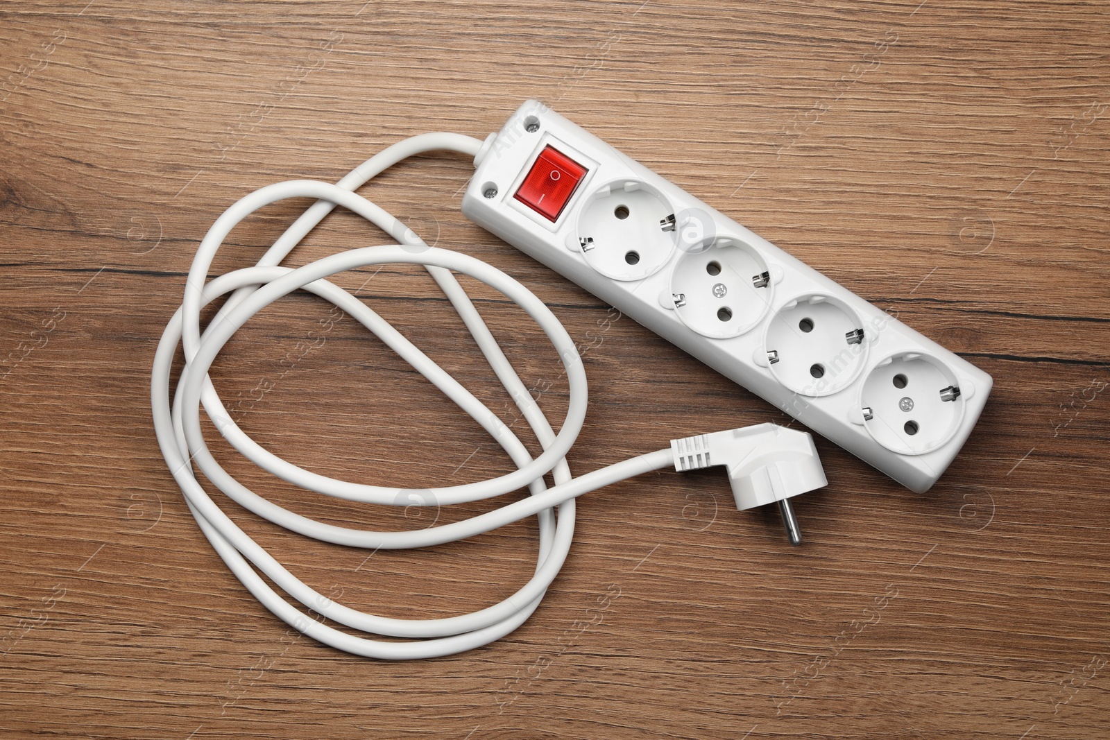 Photo of Power strip with extension cord on wooden floor, top view. Electrician's equipment