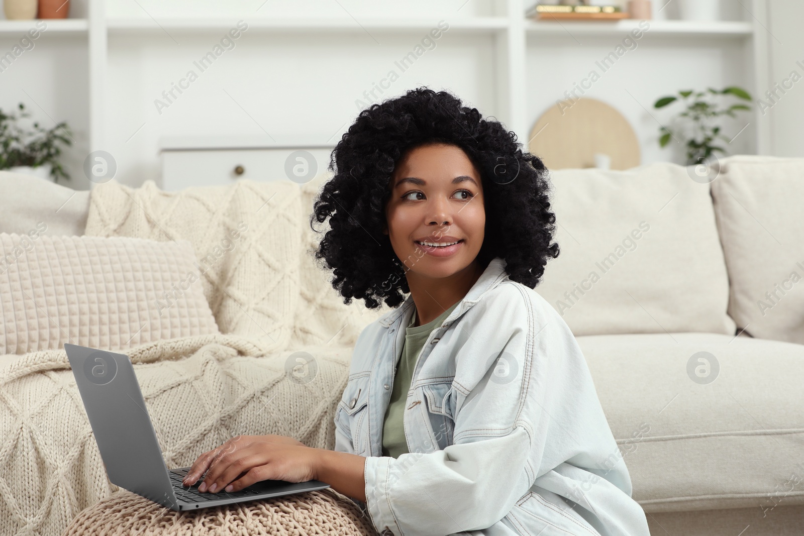 Photo of Happy young woman using laptop on pouf at home