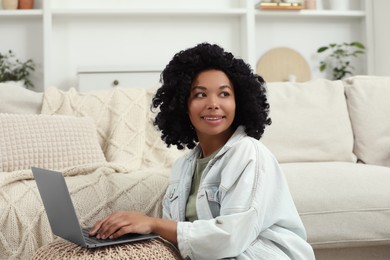 Happy young woman using laptop on pouf at home