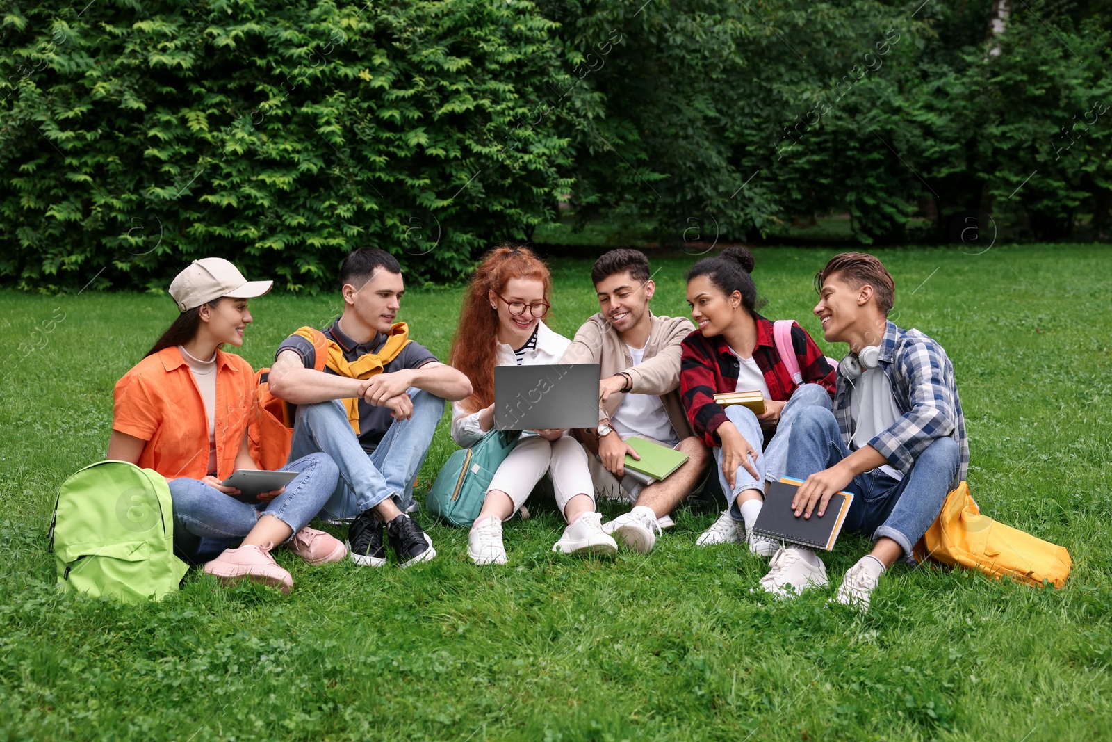 Photo of Group of happy young students learning together on green grass in park