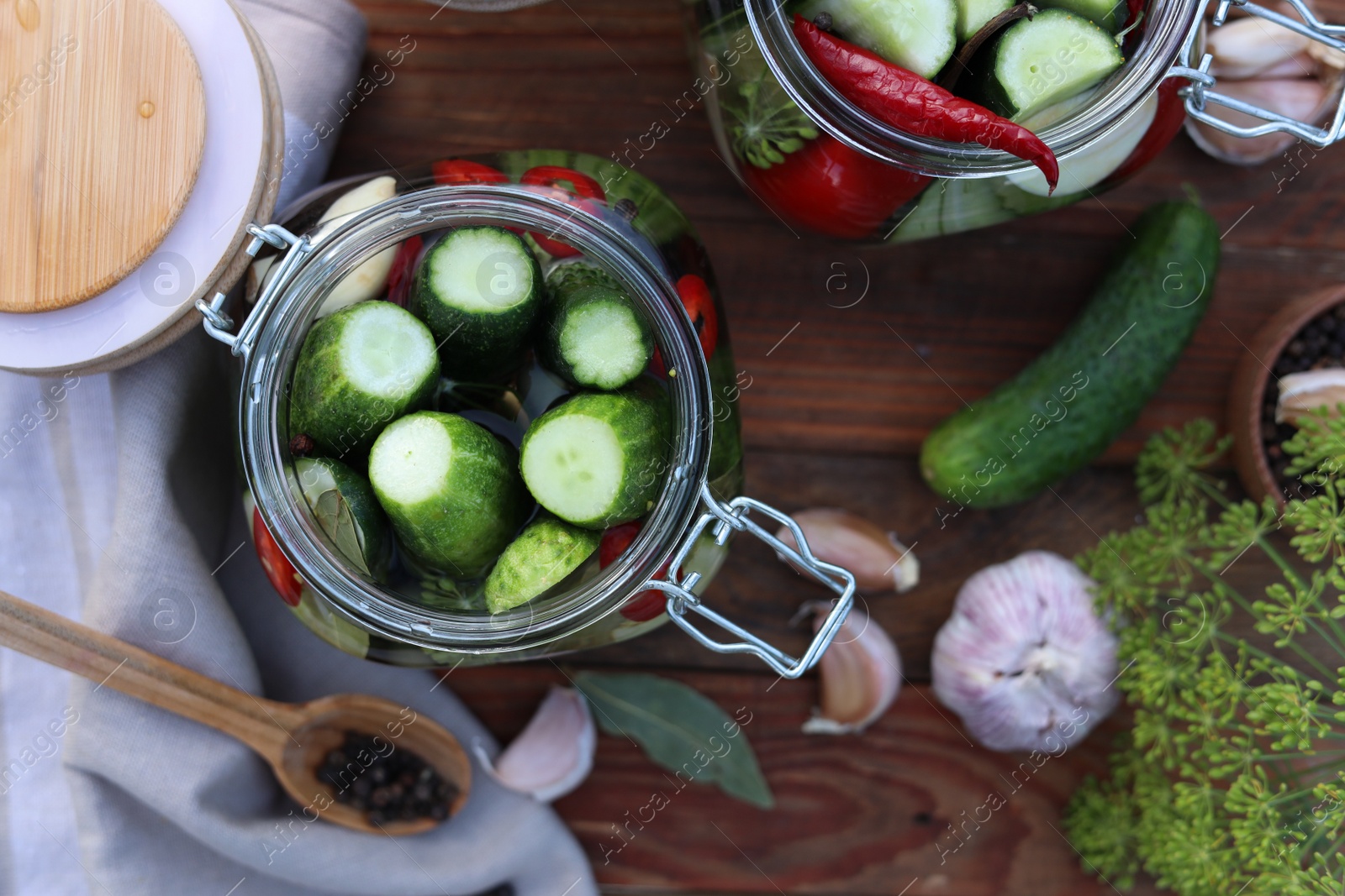 Photo of Glass jars with fresh cucumbers and other ingredients on wooden table, flat lay. Canning vegetables