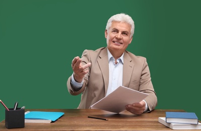 Portrait of senior teacher at table against green chalkboard