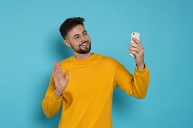 Photo of Handsome man in yellow sweatshirt with phone on light blue background