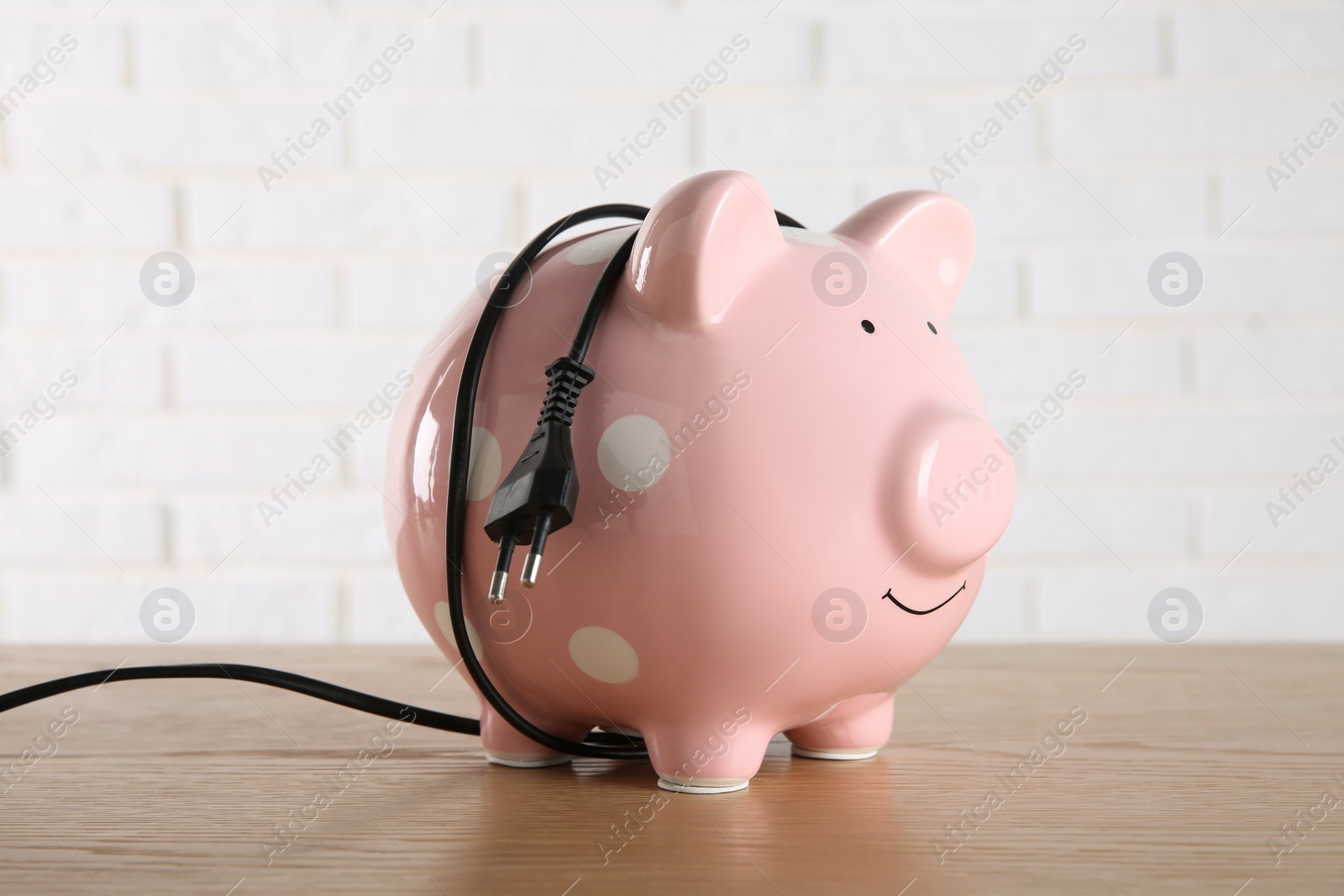 Photo of Piggy bank with power plug on wooden table. Energy saving concept
