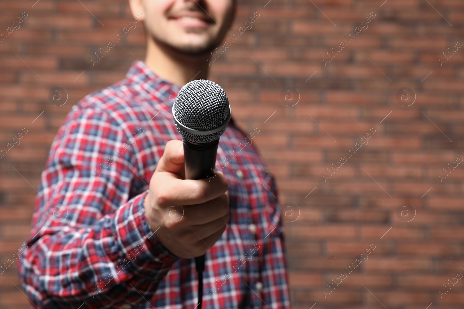 Photo of Young man in shirt holding microphone near brick wall, closeup with space for text