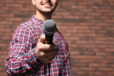 Young man in shirt holding microphone near brick wall, closeup with space for text