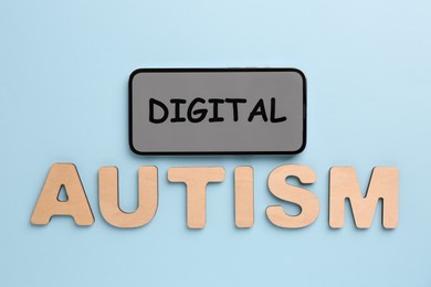 Photo of Phrase Digital Autism made of smartphone and wooden letters on light blue background, flat lay. Addictive behavior
