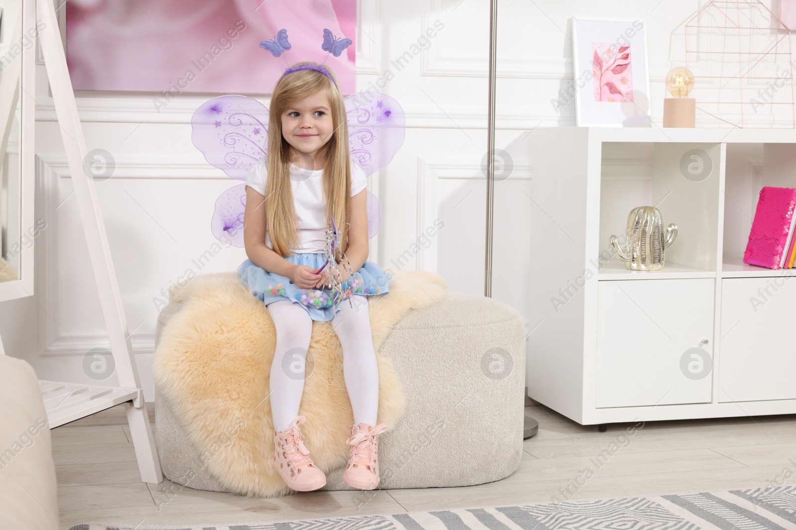 Photo of Cute little girl in fairy costume with violet wings and magic wand at home, space for text