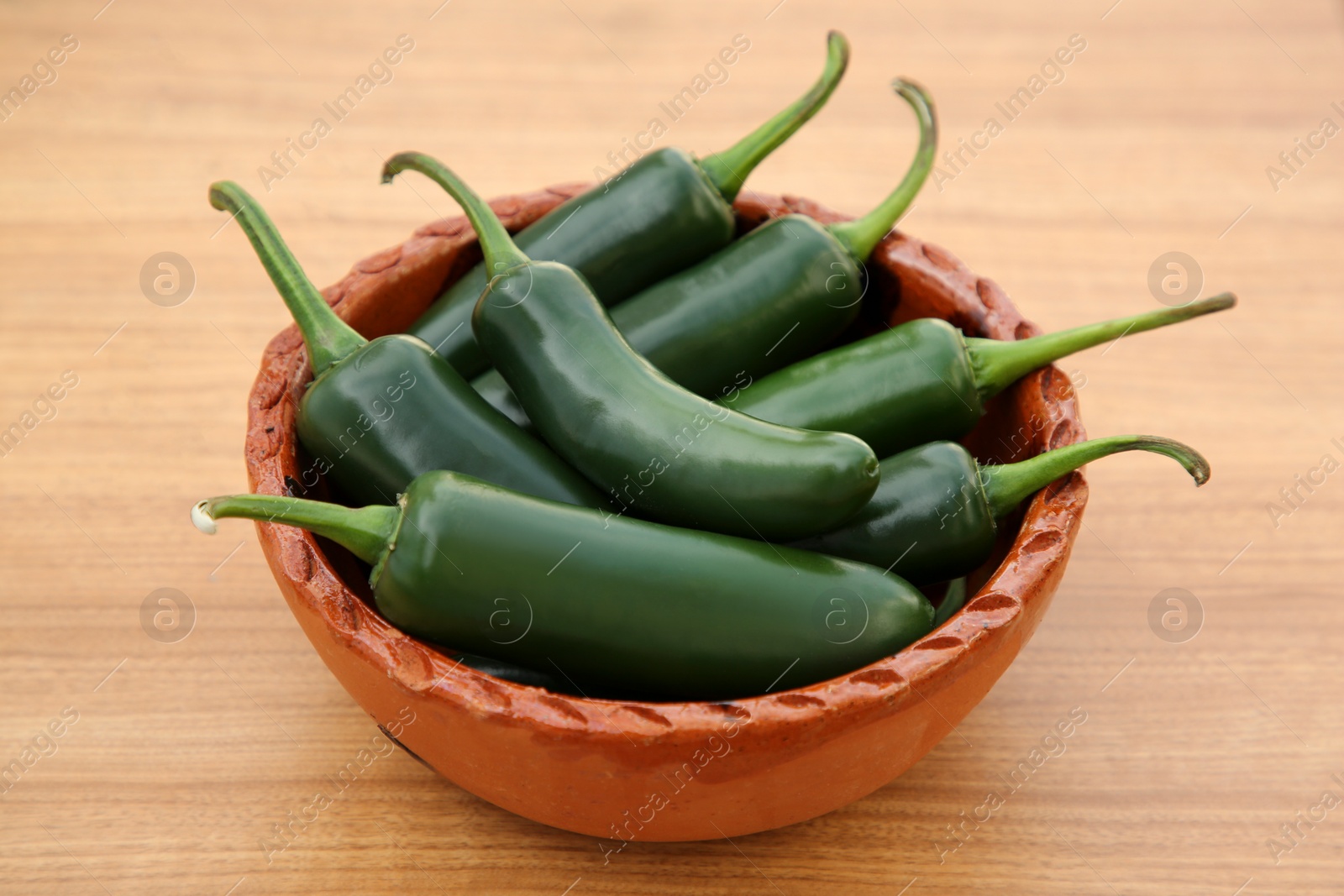 Photo of Bowl of fresh green jalapeno peppers on wooden table