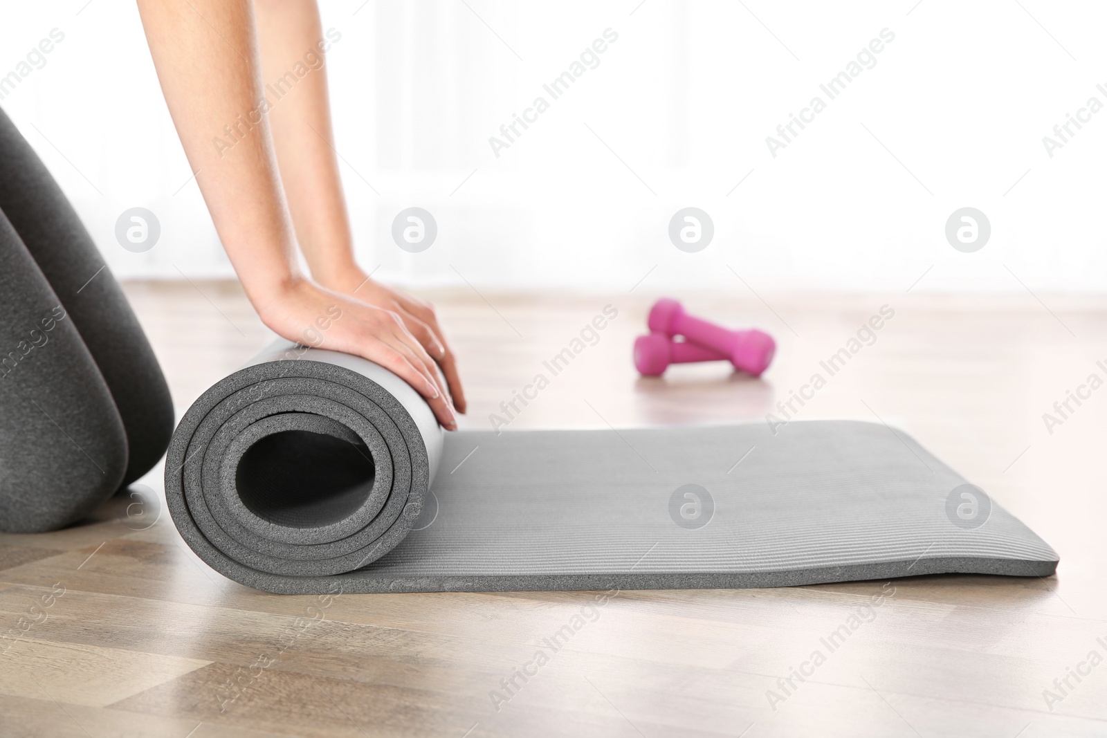 Photo of Woman rolling yoga mat on floor indoors, closeup