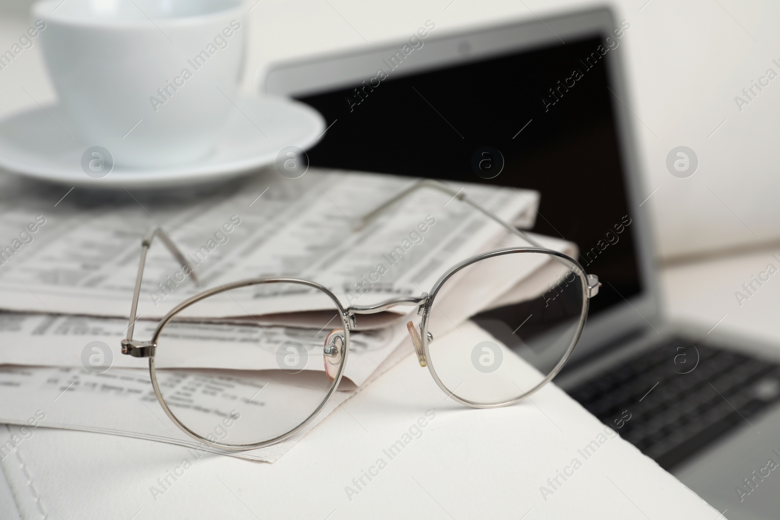 Photo of Newspapers, glasses and cup of drink on armrest indoors