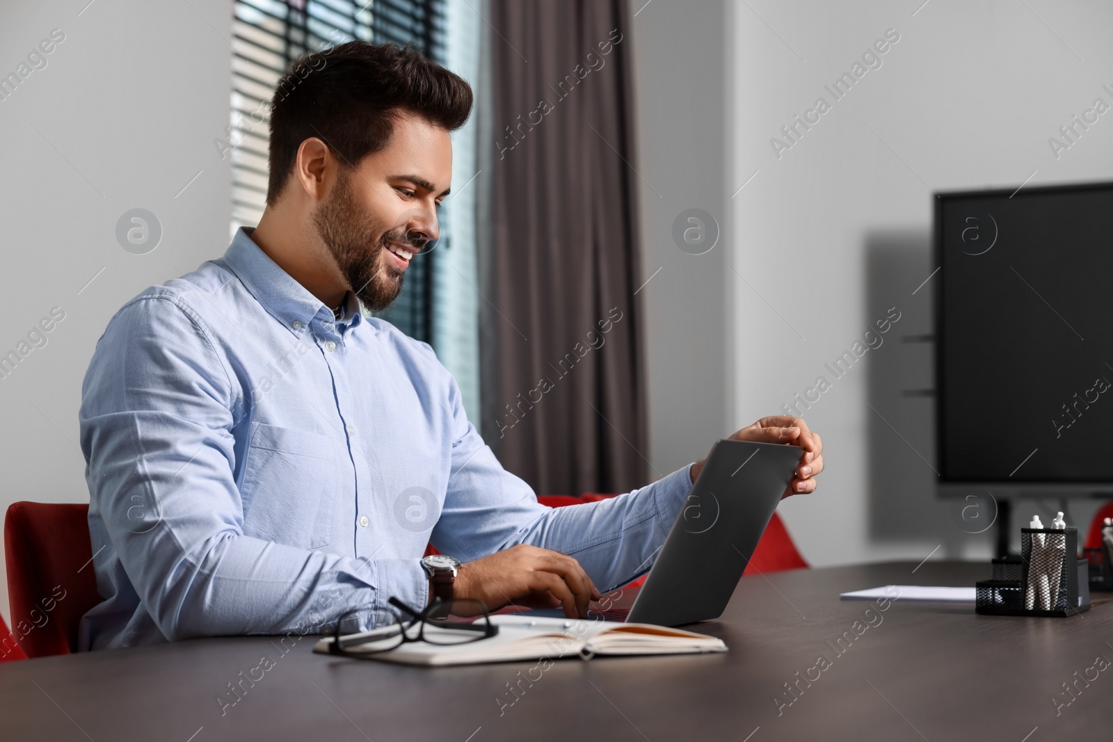 Photo of Happy young man working on laptop at table in office