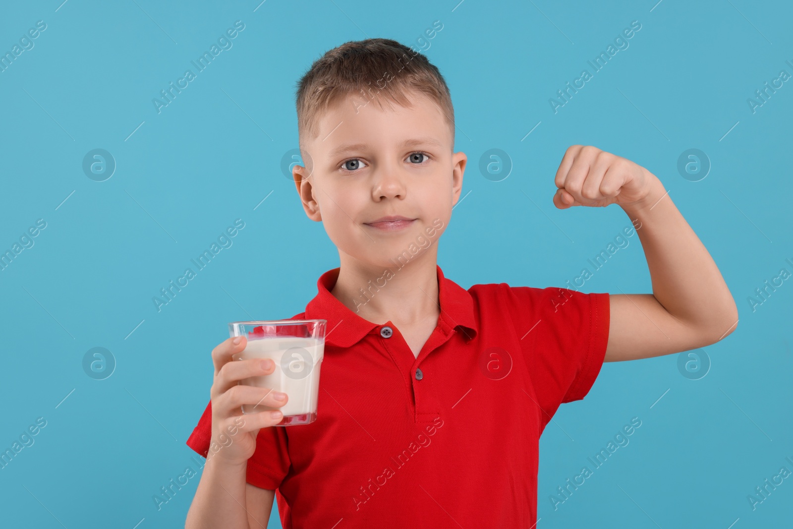 Photo of Cute boy with glass of fresh milk showing his strength on light blue background