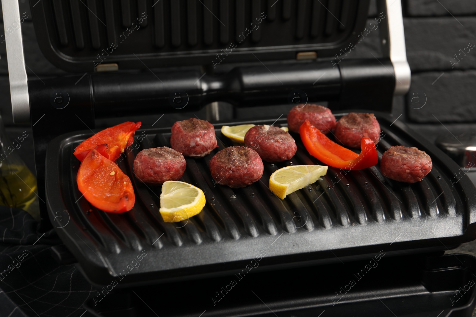 Photo of Electric grill with meat balls, bell pepper and lemon on table, closeup