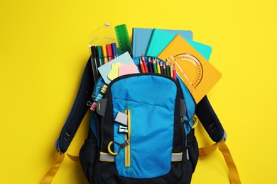 Photo of Backpack with school stationery on yellow background, top view